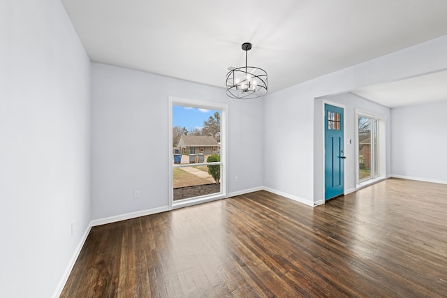 empty room with a notable chandelier, dark wood-style flooring, baseboards, and a healthy amount of sunlight