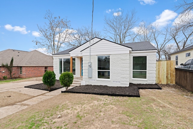 view of front of home with a shingled roof, fence, and brick siding