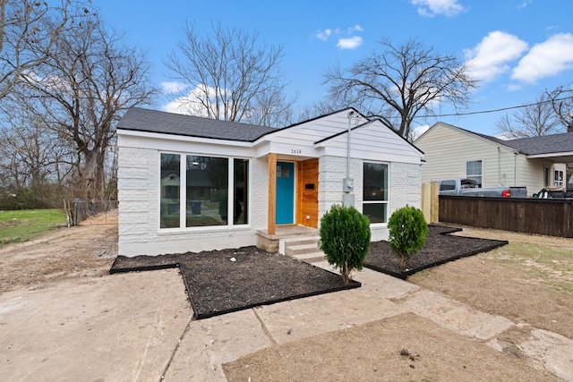 view of front of property with brick siding, a shingled roof, and fence