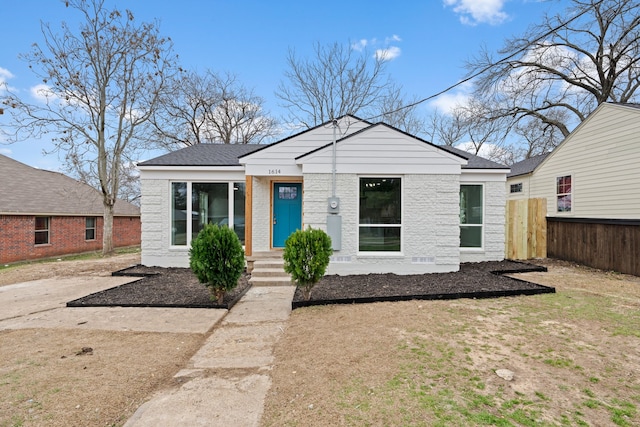 bungalow-style home with a shingled roof, brick siding, and fence