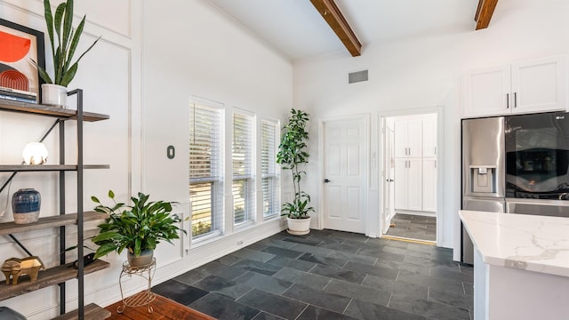 interior space featuring baseboards, visible vents, a towering ceiling, stone finish floor, and beam ceiling