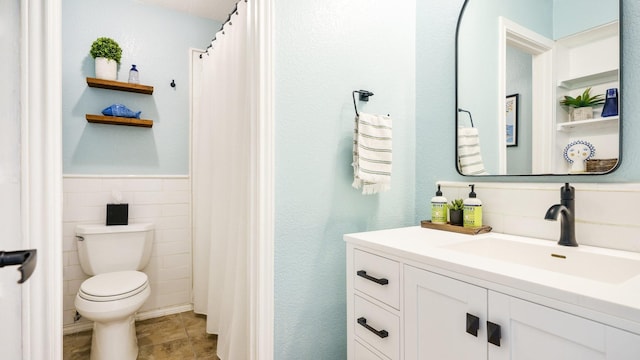 bathroom with tile walls, wainscoting, vanity, and toilet