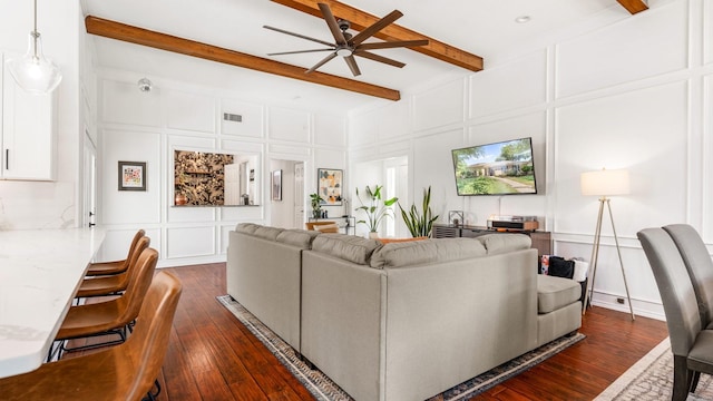 living area featuring dark wood-style flooring, a decorative wall, and beam ceiling