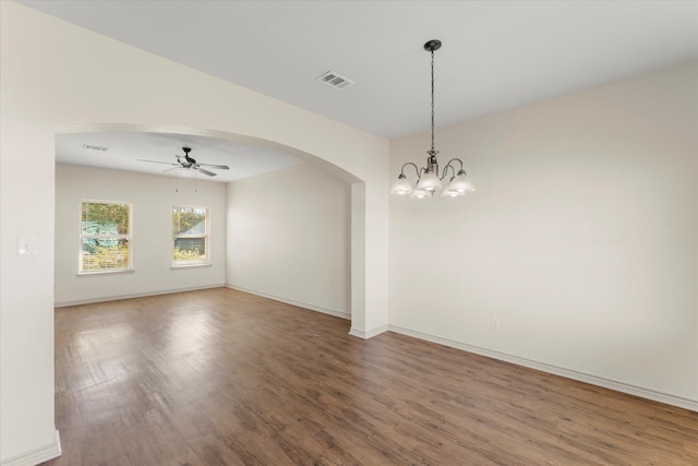 empty room with baseboards, visible vents, arched walkways, wood finished floors, and ceiling fan with notable chandelier