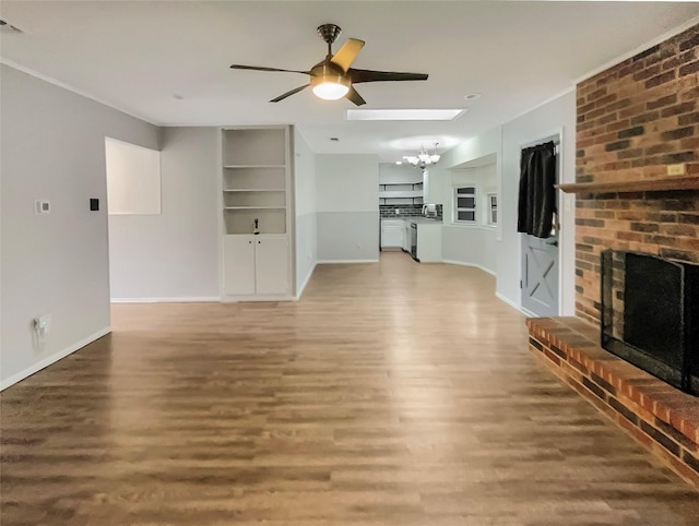 unfurnished living room featuring ceiling fan with notable chandelier, a fireplace, wood finished floors, built in features, and baseboards