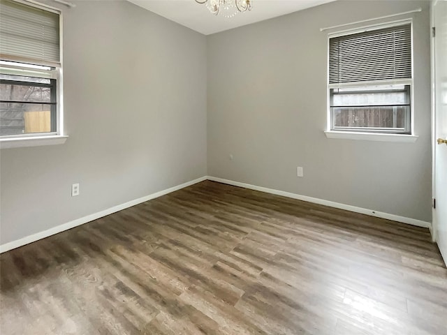 empty room with a notable chandelier, wood finished floors, and baseboards