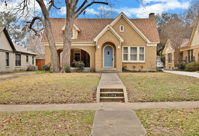 view of front facade featuring brick siding, fence, a chimney, and a front lawn