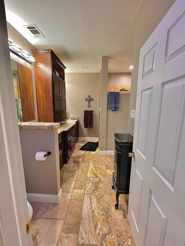 bathroom featuring baseboards, visible vents, toilet, a textured ceiling, and vanity