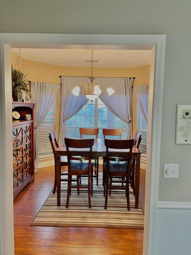 dining space with wood finished floors, a wainscoted wall, visible vents, and an inviting chandelier