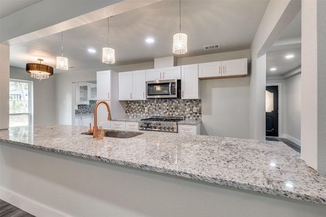 kitchen featuring white cabinets, stainless steel microwave, light stone countertops, pendant lighting, and a sink