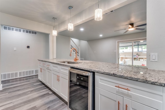 kitchen featuring beverage cooler, visible vents, white cabinets, pendant lighting, and a sink