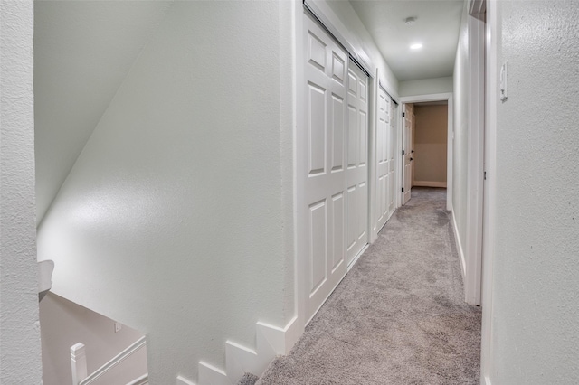 corridor featuring baseboards, a textured wall, and light colored carpet