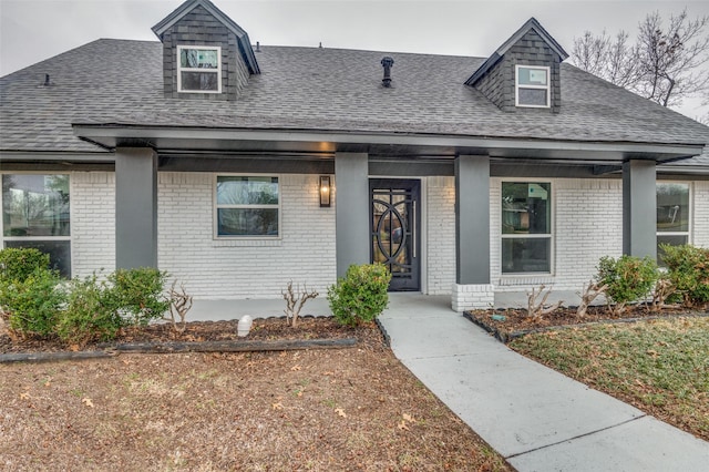 view of front of house with covered porch, a shingled roof, and brick siding