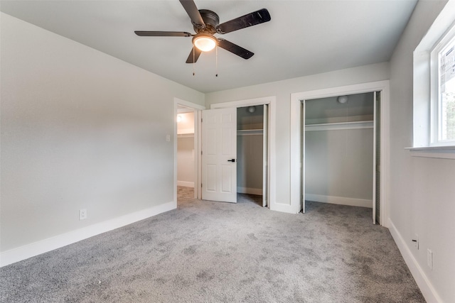 unfurnished bedroom with light carpet, ceiling fan, two closets, and baseboards