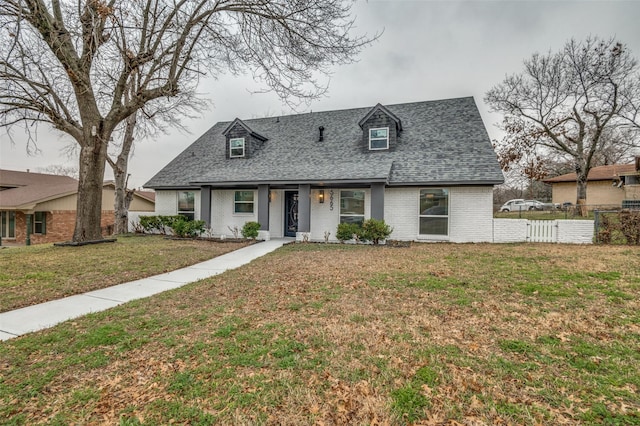 view of front facade featuring brick siding, roof with shingles, a front yard, and fence