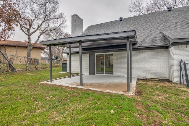 rear view of property featuring brick siding, roof with shingles, a chimney, a lawn, and a patio area