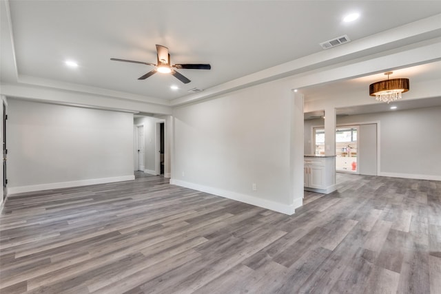 empty room featuring light wood finished floors, baseboards, visible vents, and ceiling fan with notable chandelier