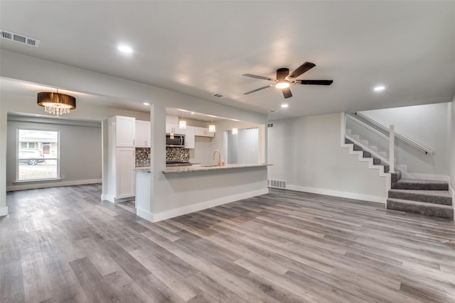 kitchen with stainless steel microwave, visible vents, light wood-style flooring, white cabinetry, and light stone countertops