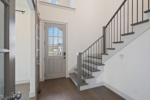 foyer featuring a barn door, baseboards, dark wood finished floors, a towering ceiling, and stairway