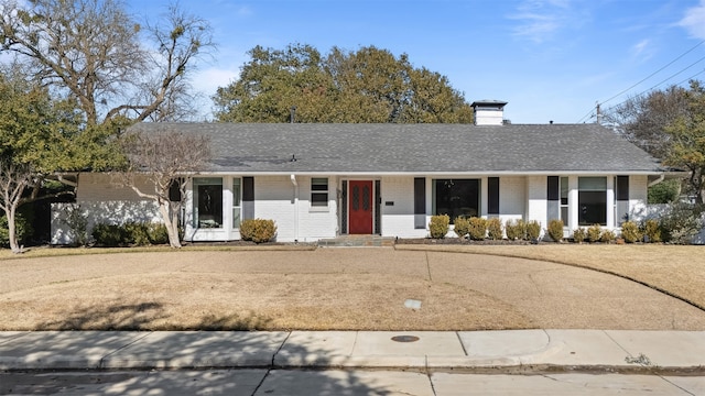 ranch-style house featuring roof with shingles, a chimney, and brick siding