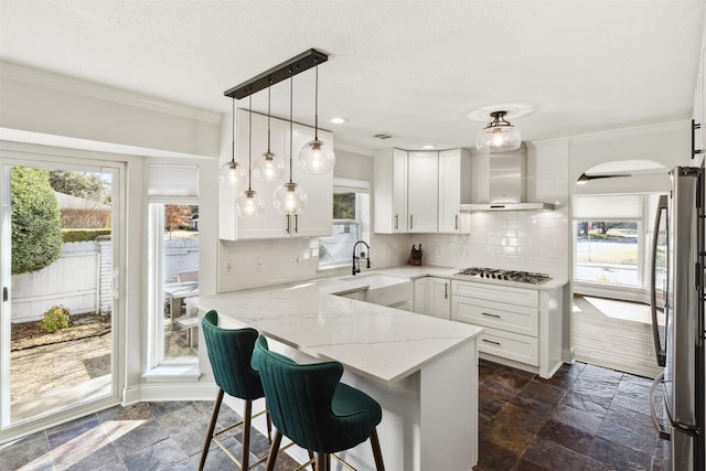 kitchen featuring wall chimney exhaust hood, light stone counters, stone tile flooring, and white cabinetry