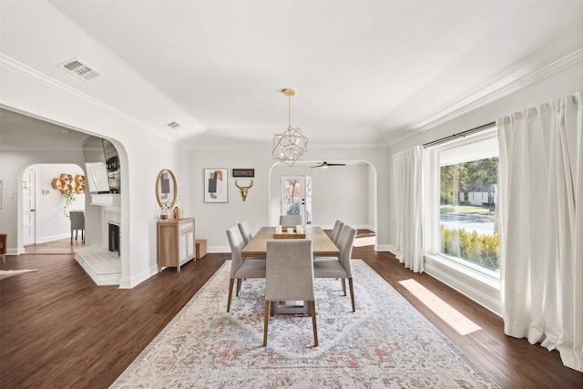 dining space featuring visible vents, arched walkways, a fireplace with raised hearth, ornamental molding, and dark wood-style flooring