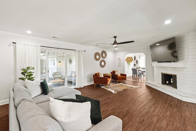 living room featuring baseboards, arched walkways, ornamental molding, dark wood-style flooring, and a fireplace