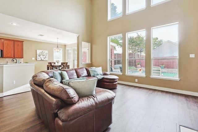 living area featuring a towering ceiling, baseboards, crown molding, and wood finished floors