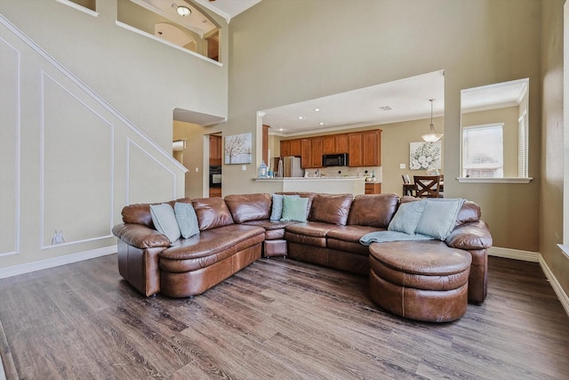 living room featuring a towering ceiling, baseboards, wood finished floors, and ornamental molding