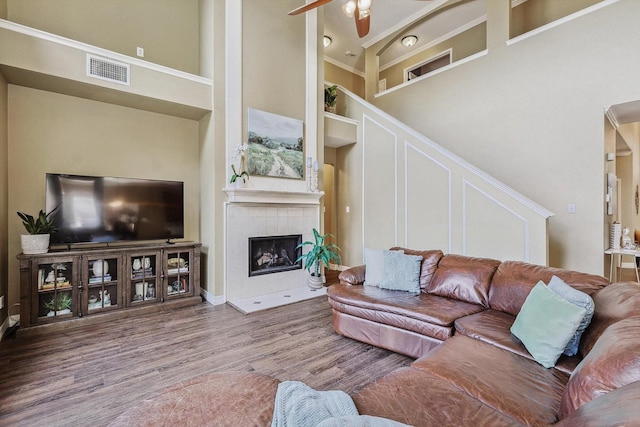 living area with ceiling fan, a tile fireplace, wood finished floors, a towering ceiling, and visible vents