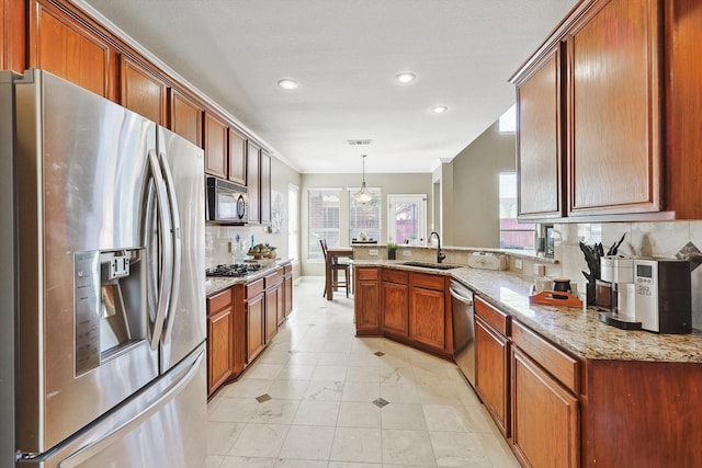 kitchen featuring light stone counters, pendant lighting, brown cabinets, stainless steel appliances, and a sink