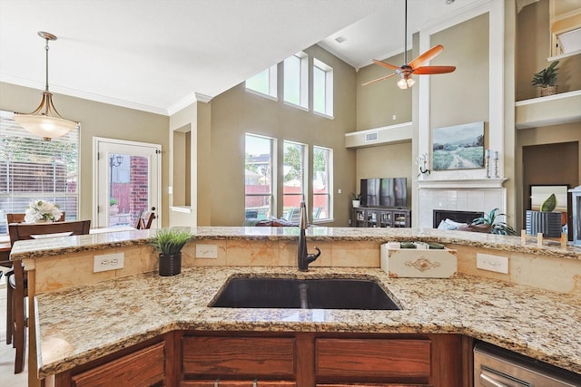 kitchen with light stone counters, a tile fireplace, a sink, open floor plan, and hanging light fixtures