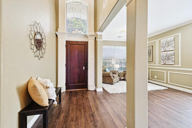 foyer entrance featuring crown molding, decorative columns, a decorative wall, and wood finished floors