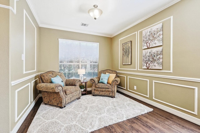 sitting room with crown molding, visible vents, a decorative wall, and wood finished floors