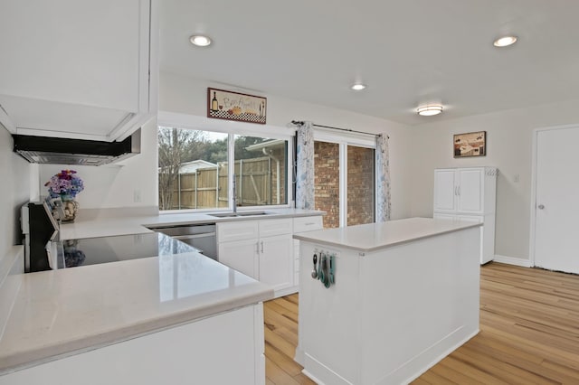 kitchen with light countertops, a kitchen island, white cabinetry, and light wood-style floors