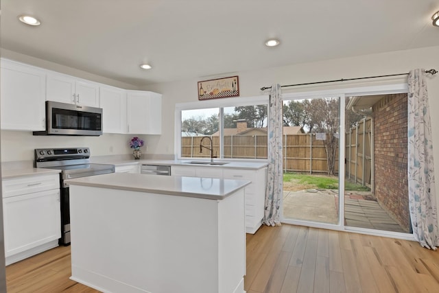 kitchen with light countertops, appliances with stainless steel finishes, white cabinetry, a kitchen island, and a sink