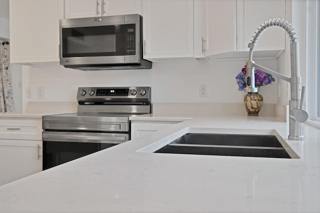 kitchen featuring stainless steel appliances, light stone counters, a sink, and white cabinets