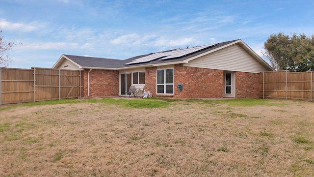 rear view of property with solar panels, brick siding, a lawn, and a fenced backyard