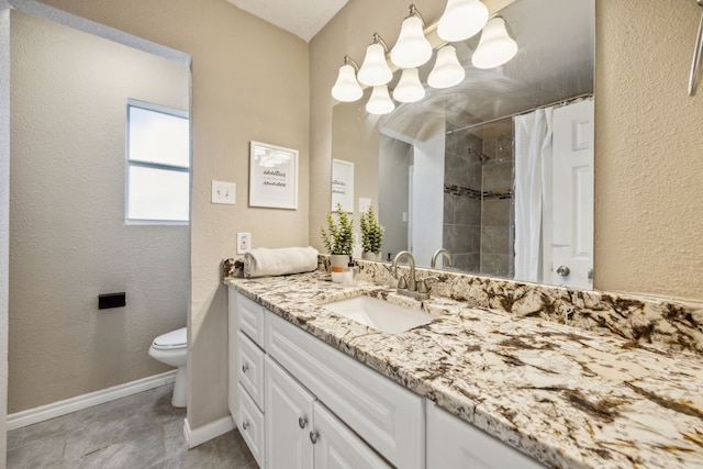 bathroom featuring a textured wall, toilet, vanity, baseboards, and tiled shower