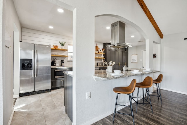 kitchen with light stone counters, open shelves, stainless steel appliances, tasteful backsplash, and island range hood