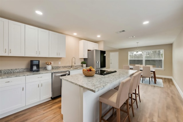 kitchen featuring a sink, a kitchen island, white cabinetry, appliances with stainless steel finishes, and pendant lighting