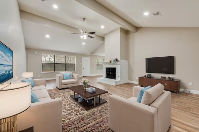 living area with baseboards, a ceiling fan, a glass covered fireplace, lofted ceiling with beams, and light wood-style flooring