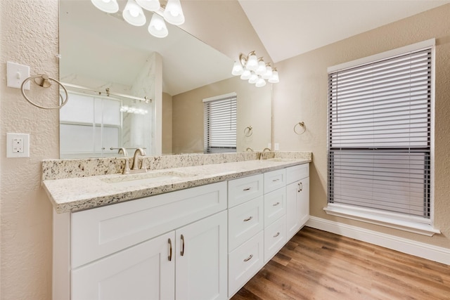 full bathroom featuring wood finished floors, vaulted ceiling, a sink, and double vanity