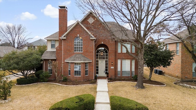 traditional home featuring central air condition unit, brick siding, a shingled roof, a chimney, and a front yard