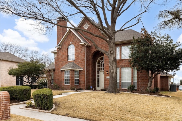 view of front of house featuring a front yard, brick siding, a chimney, and central AC unit