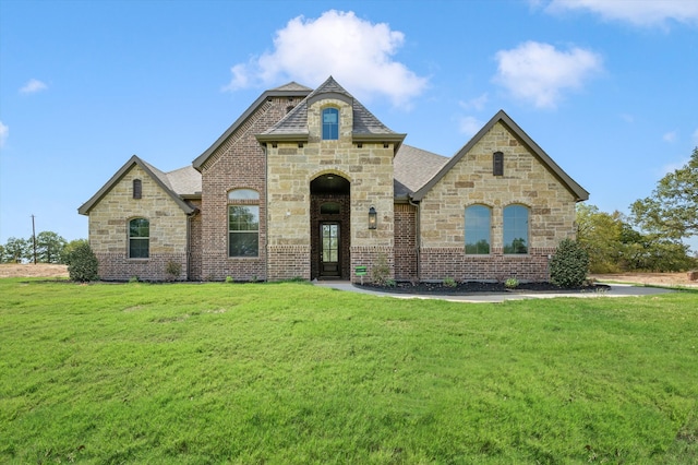 french provincial home featuring a front lawn, roof with shingles, and brick siding