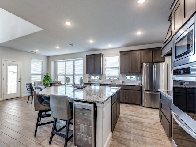 kitchen featuring a center island, a sink, stainless steel appliances, dark brown cabinetry, and wine cooler