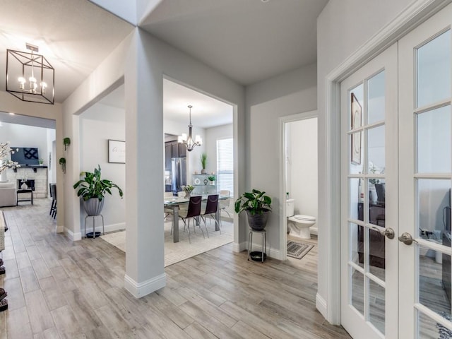 foyer entrance with light wood-style flooring, baseboards, a notable chandelier, and french doors