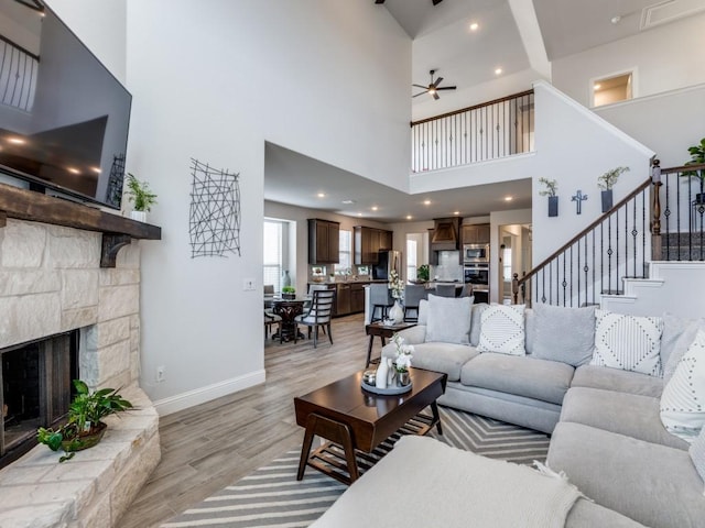 living room with a fireplace, a ceiling fan, light wood-type flooring, baseboards, and stairs