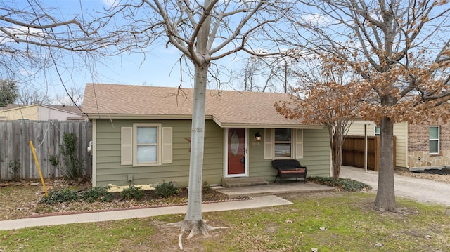 view of front of home with roof with shingles, a front yard, and fence